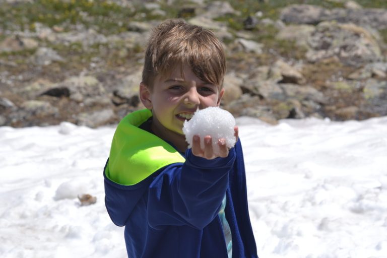 Young boy holding snow in Rocky Mountains on family vacation