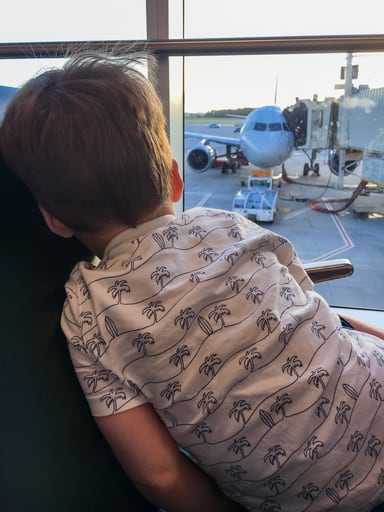 Child looking out airport window at airplane