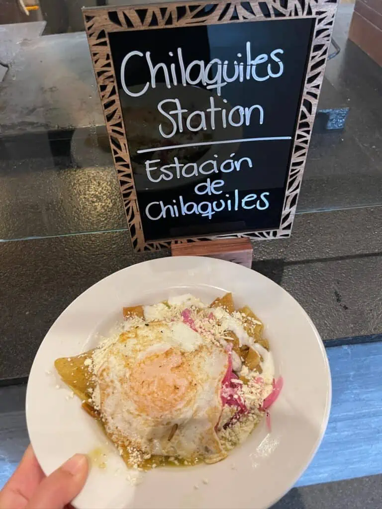 A plate full of Chilaquiles in front of a sign that says Chilaquiles Station from buffet at all-inclusive resort in Mexico
