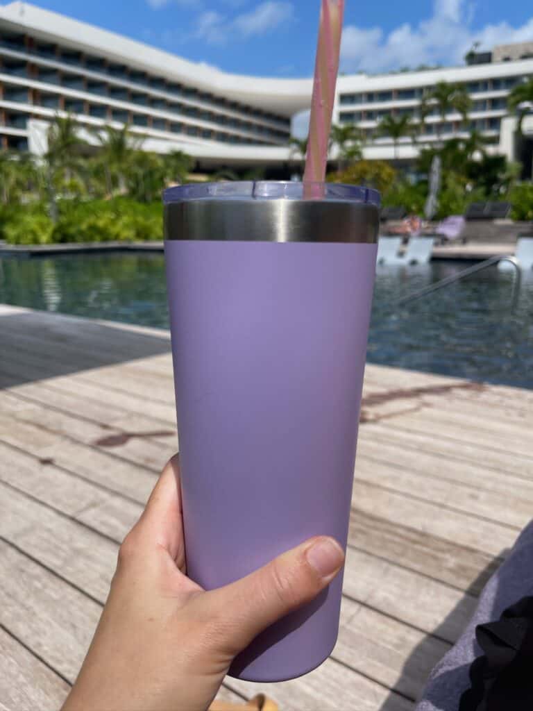 Purple insulated cup with pink straw in front of a pool at all-inclusive resort