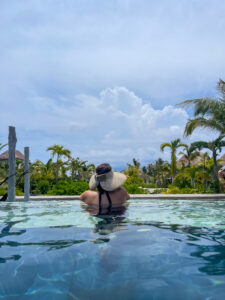 Back of woman in wide brimmed hat looking over edge of infinity pool.