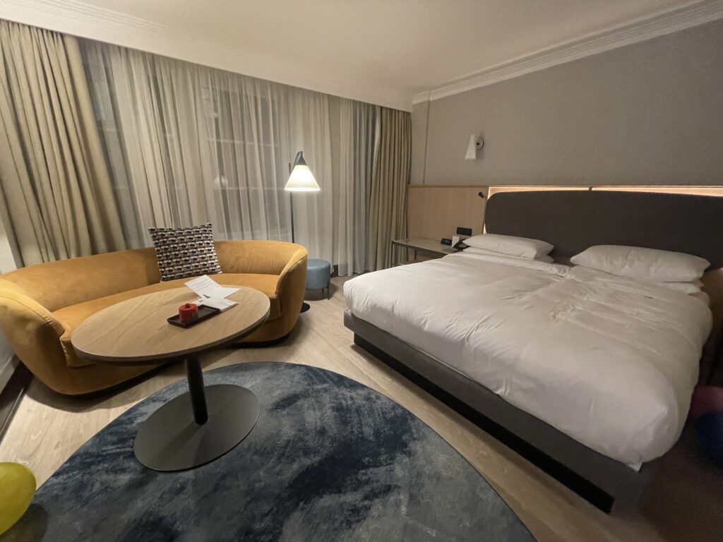 Hyatt Regency London Blackfriars standard King room with bed and yellow couch with round table.