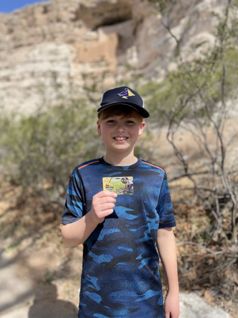 child holding national parks "America the Beautiful" pass standing in a national park.
