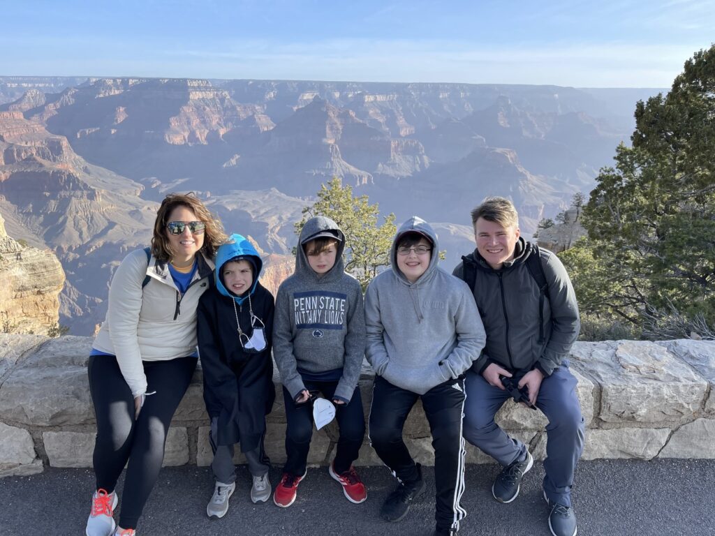 Family of 5 with 3 boys sitting on rock ledge with Grand Canyon in the background.